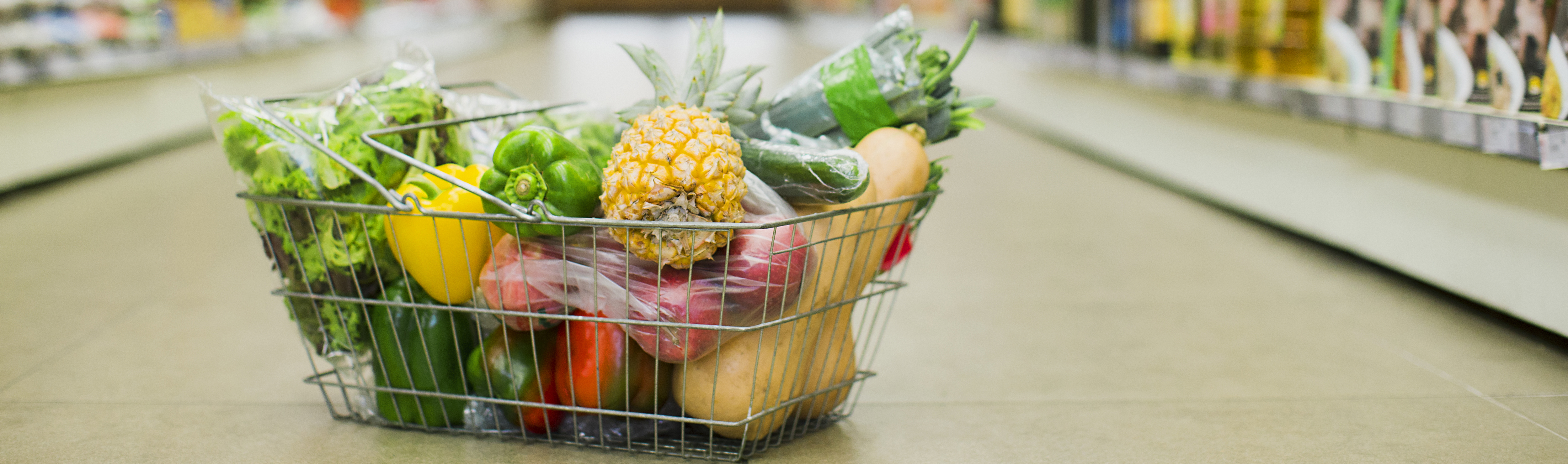 Image of a grocery basket sitting in the aisle that is filled with fruits and vegetables